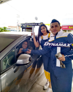Promotoras de Dynamax realizando experiencia BTL con cliente junto a vehículo en punto de atención automotriz