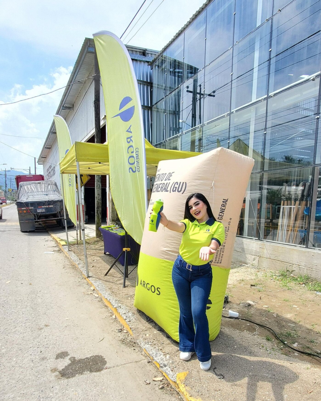Edecán de marca Argos en activación BTL exterior junto a exhibición de cemento y bandera publicitaria.