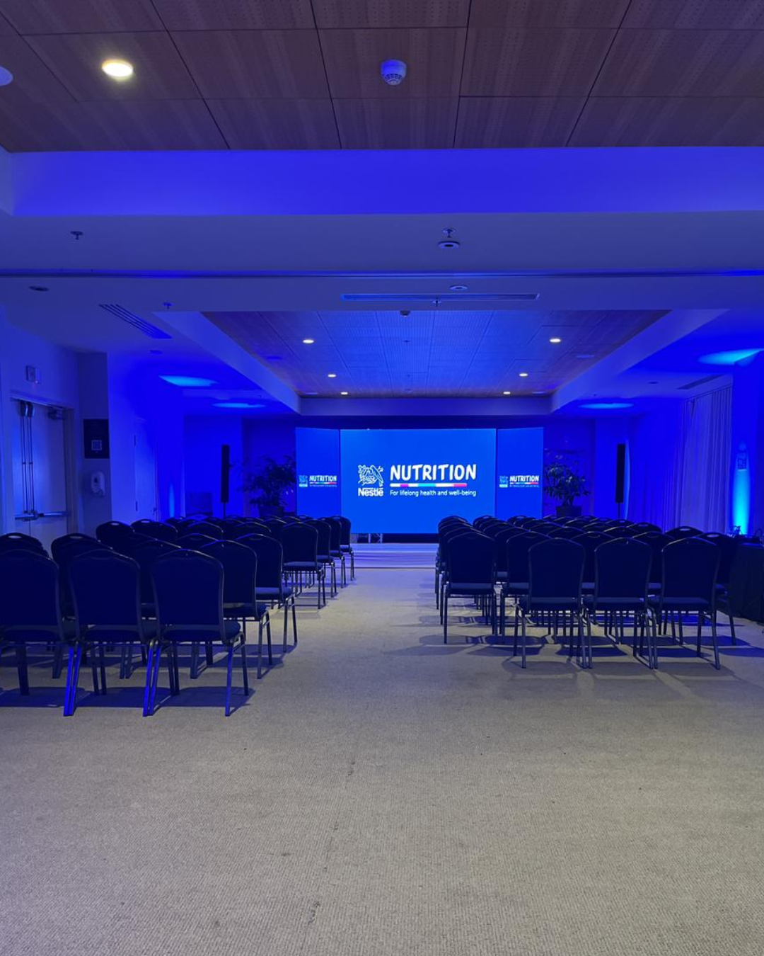 Salón preparado para conferencia corporativa de Nestlé Nutrition en Honduras con escenario iluminado y sillas para asistentes