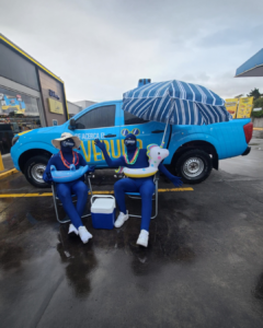 Promotores en experiencia BTL de verano junto a instalación inflable azul y vehículo promocional en estación de servicio UNO