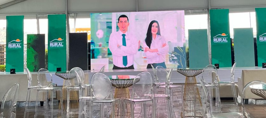 Montaje de evento corporativo de Caja Rural en Honduras con pantalla principal, mobiliario transparente y ambientación de marca