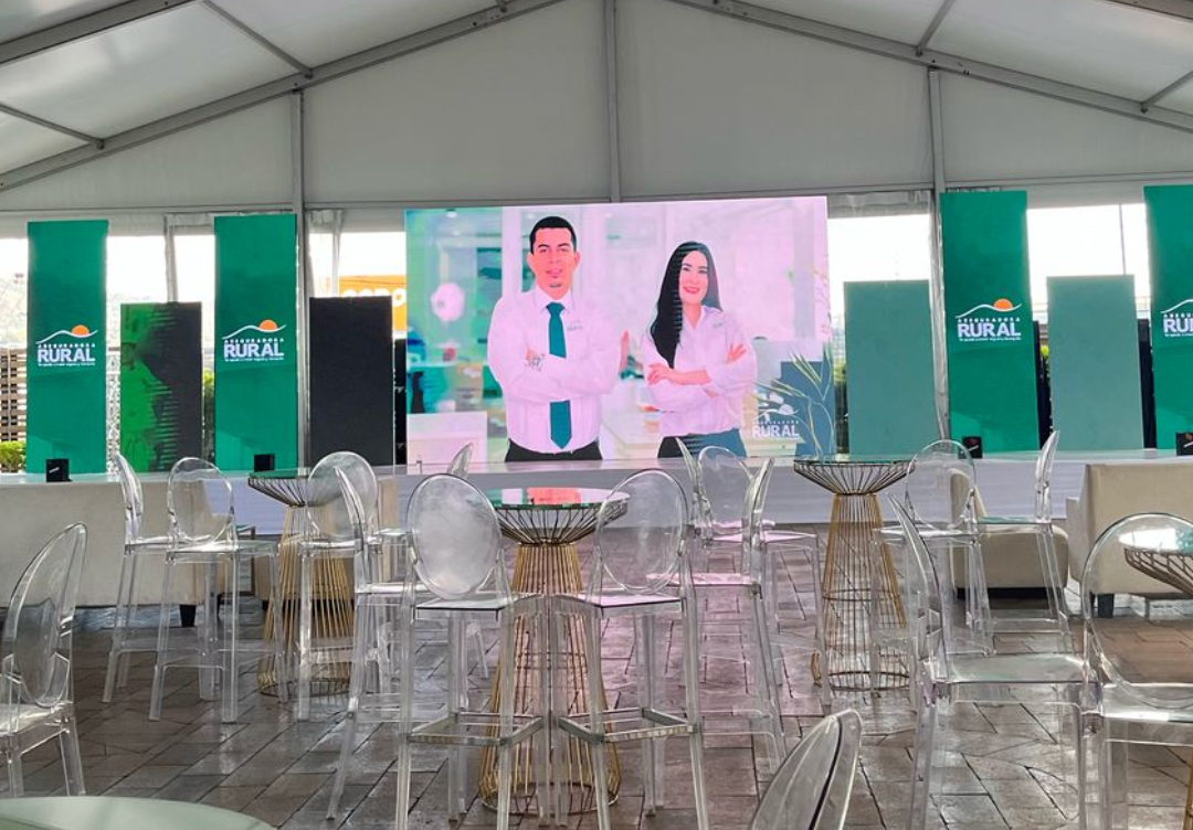 Montaje de evento corporativo de Caja Rural en Honduras con pantalla principal, mobiliario transparente y ambientación de marca