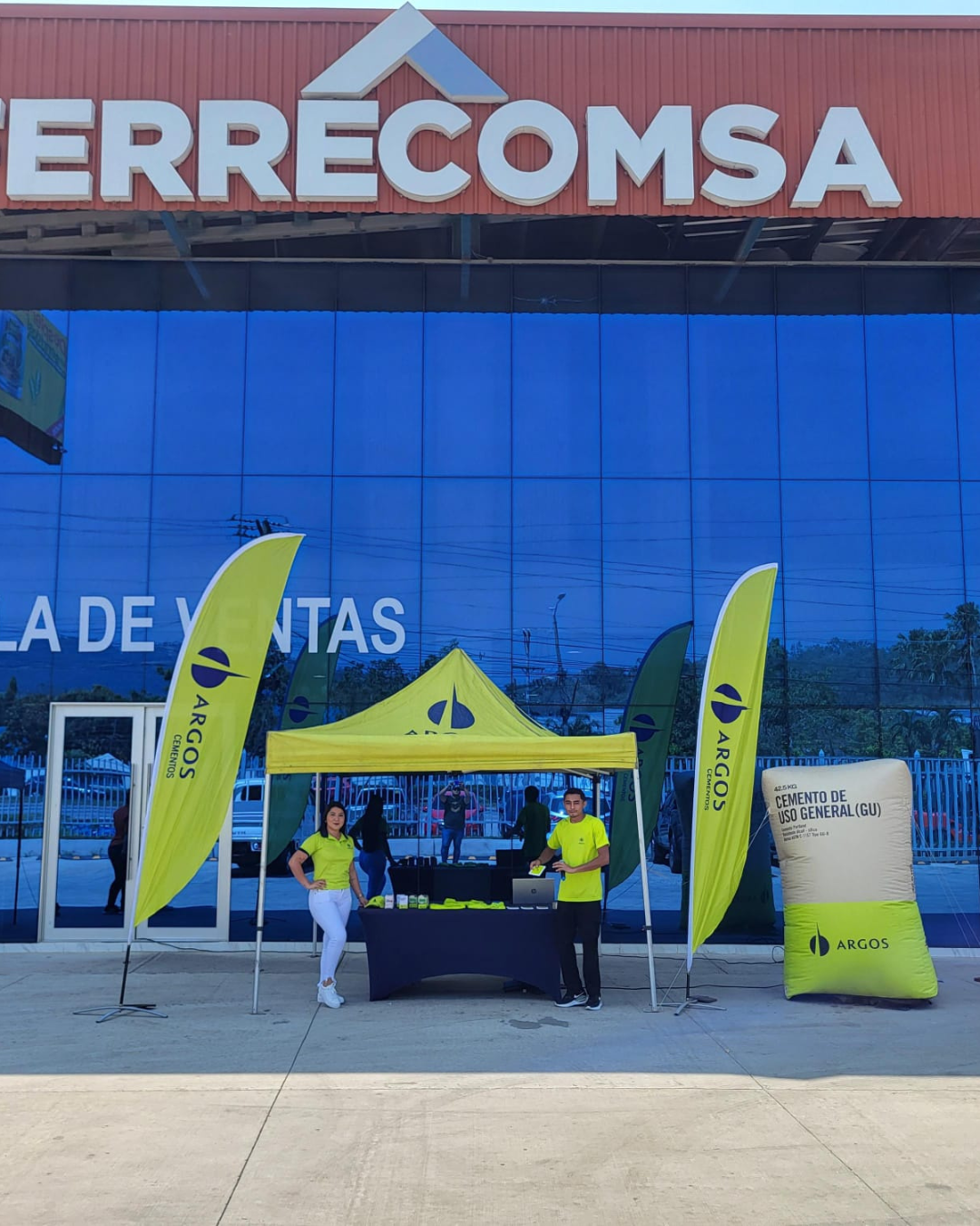 Stand promocional de Argos frente a tienda ERRECOMSA con carpa y banderas publicitarias para activación BTL.
