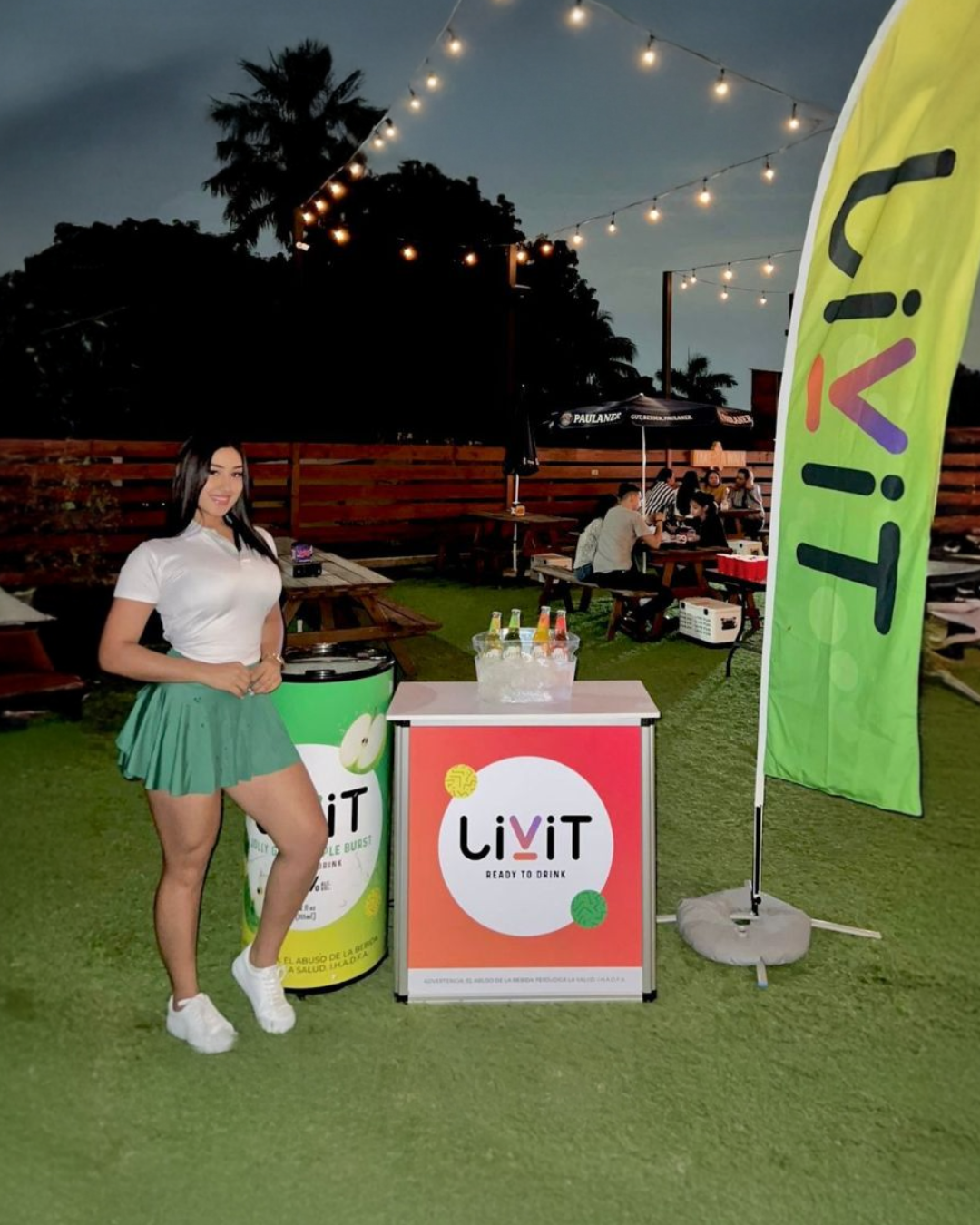 Edecán de marca Livit en activación BTL exterior con stand, bandera publicitaria y exhibición promocional.